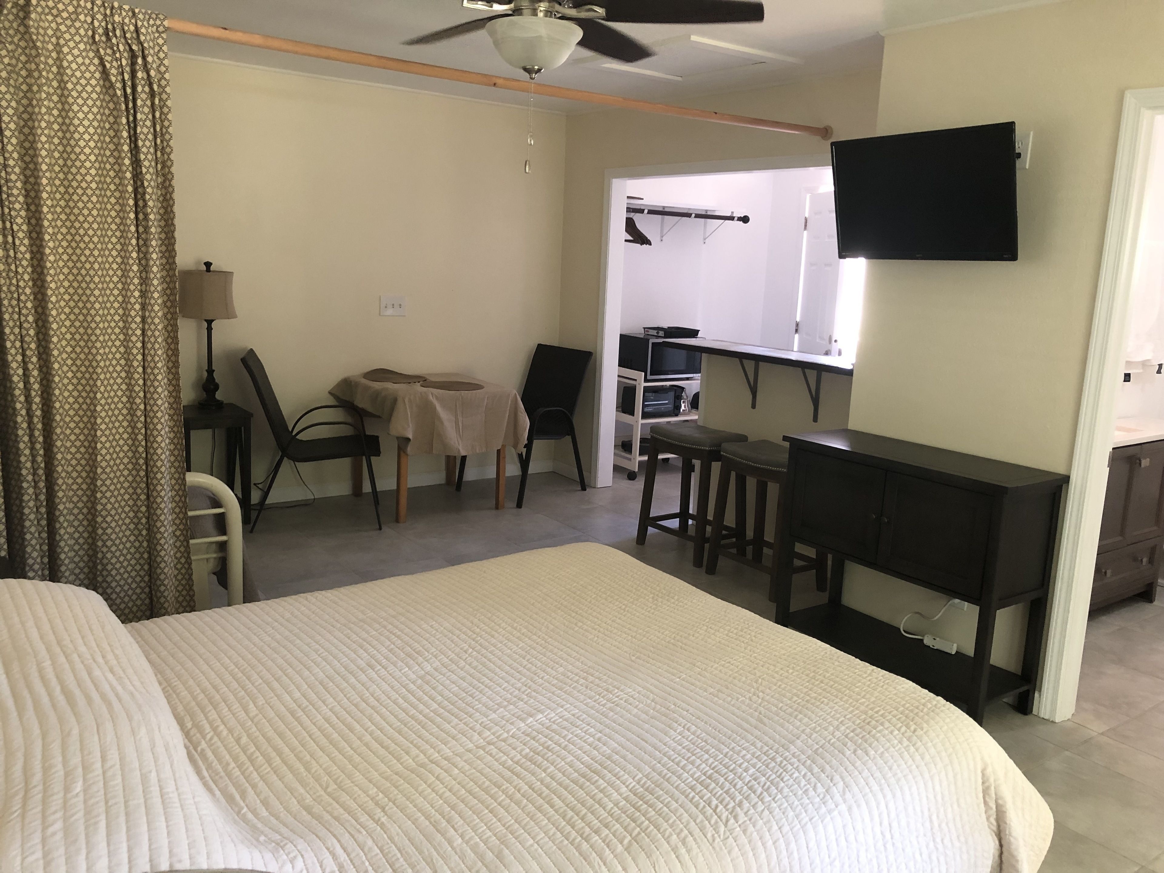 A hotel room with a bed, a desk, a chair, a small table, and a TV mounted on the wall.