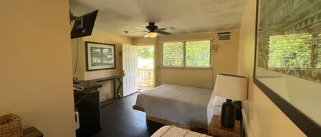 A bedroom with a bed, a desk, a chair, a ceiling fan, and a window with blinds.