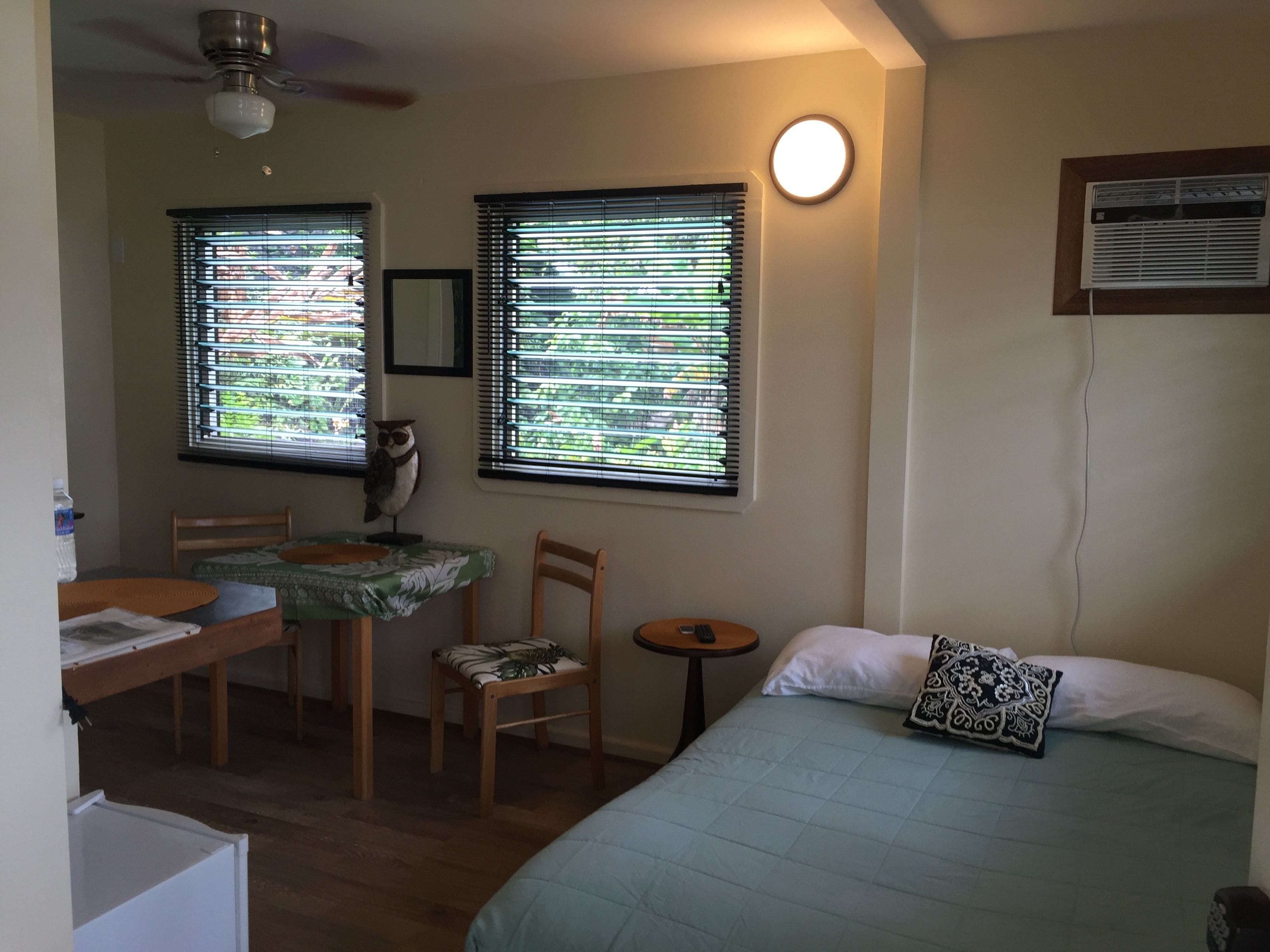 A room with a bed, a desk, a chair, and two windows with blinds.