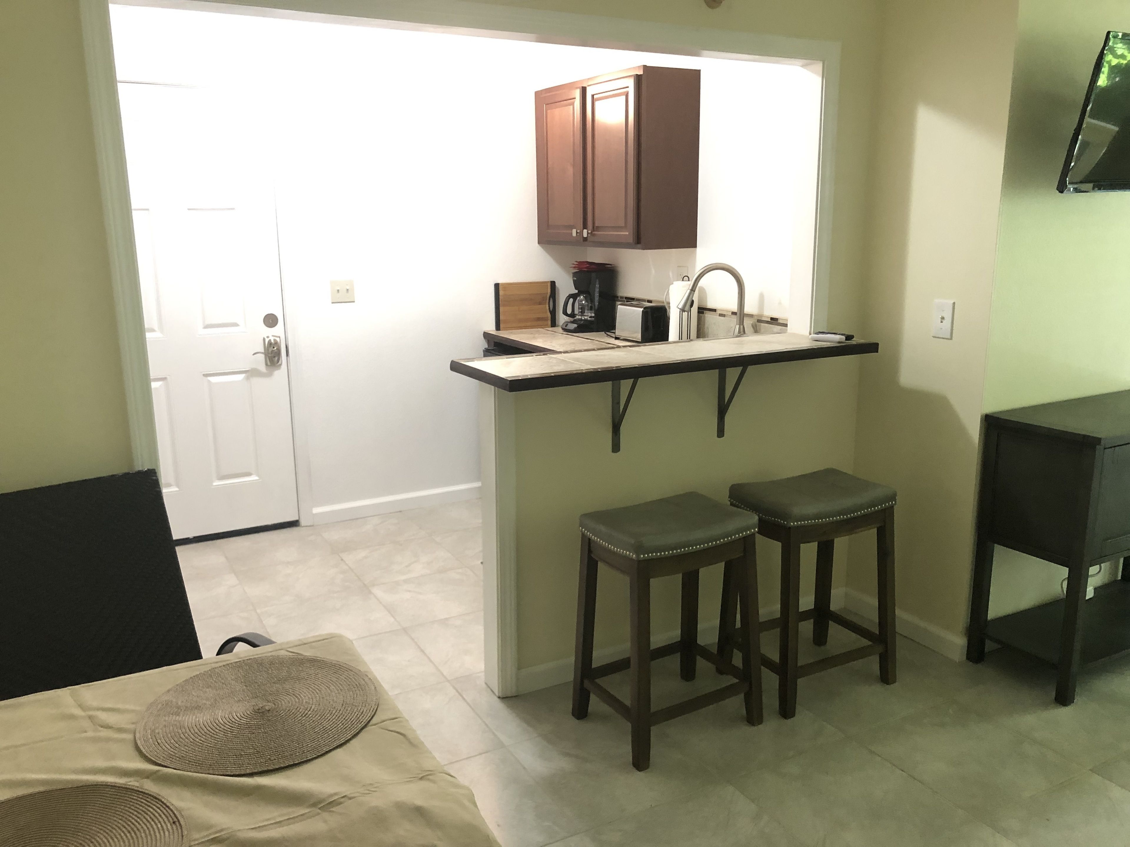 A compact kitchen with a countertop, two stools, and a small table.