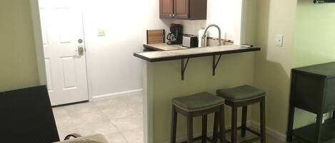 A compact kitchen with a countertop, two stools, and a small table.