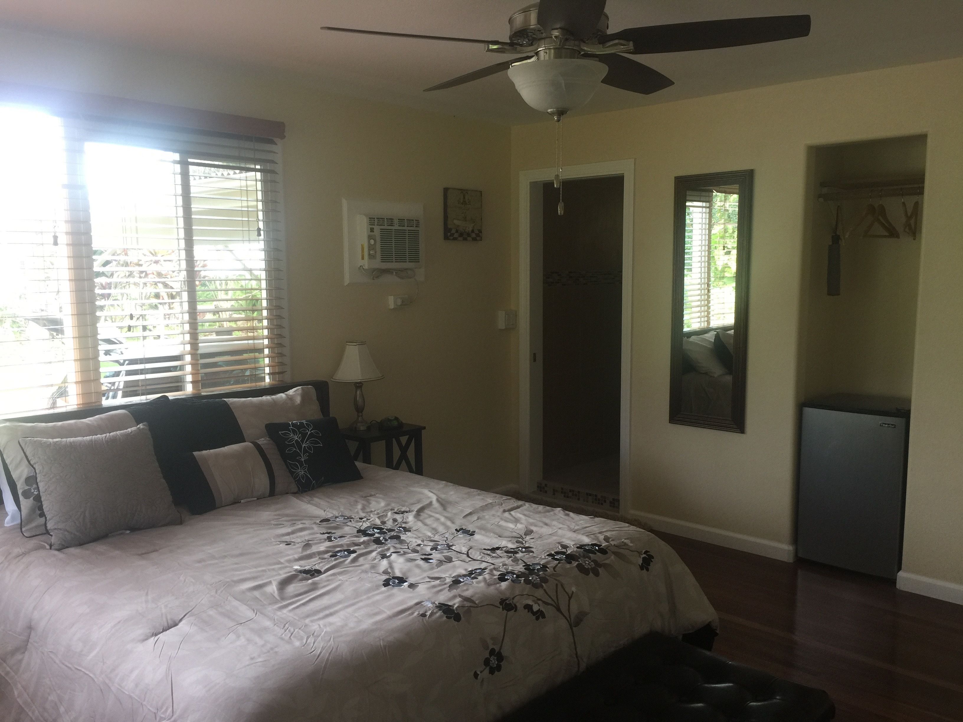 A bedroom with a bed, a ceiling fan, a nightstand, a lamp, a dresser, and a window with blinds.