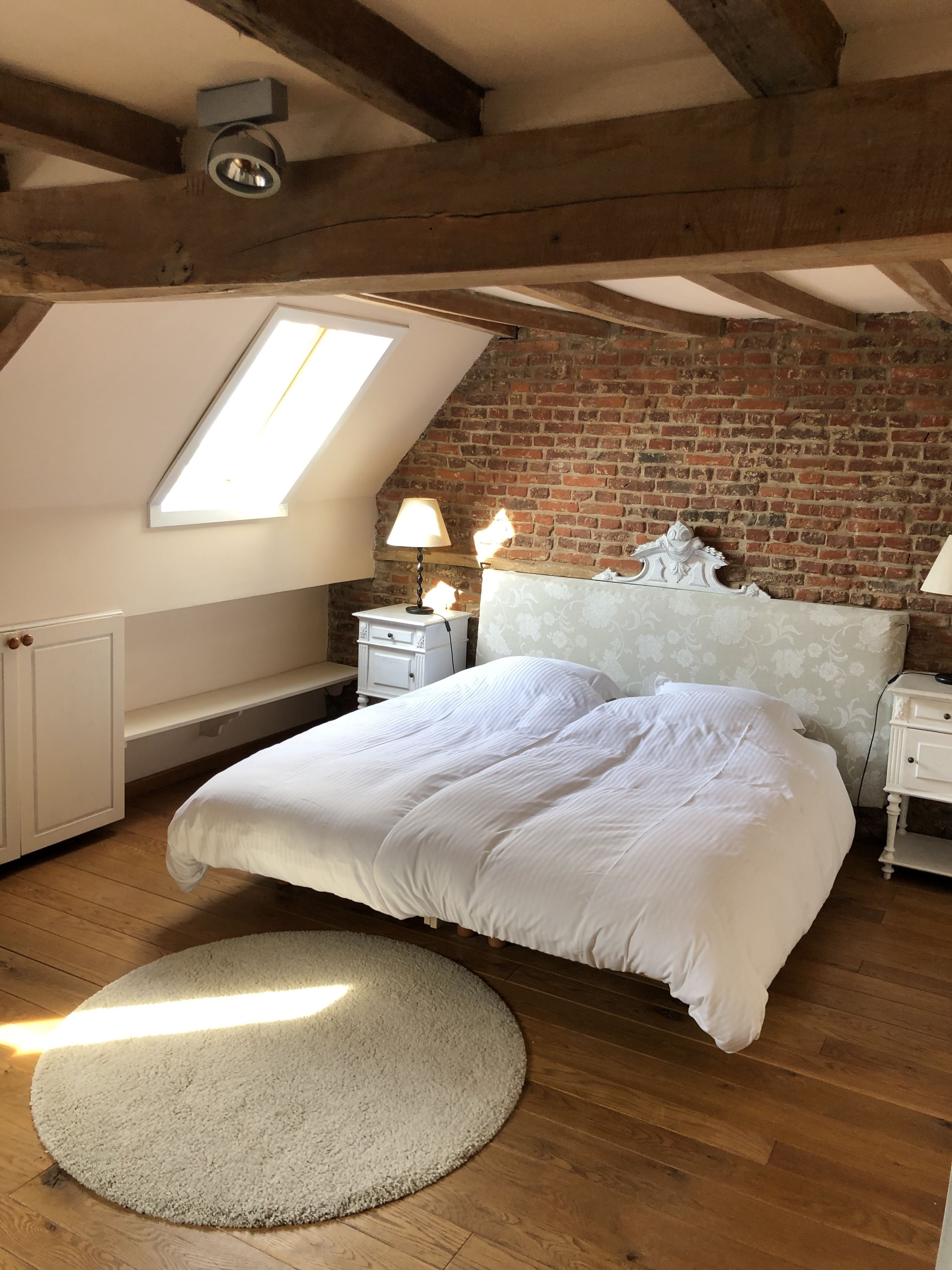 A bedroom with a large bed, a skylight, a brick wall, and a wooden floor.