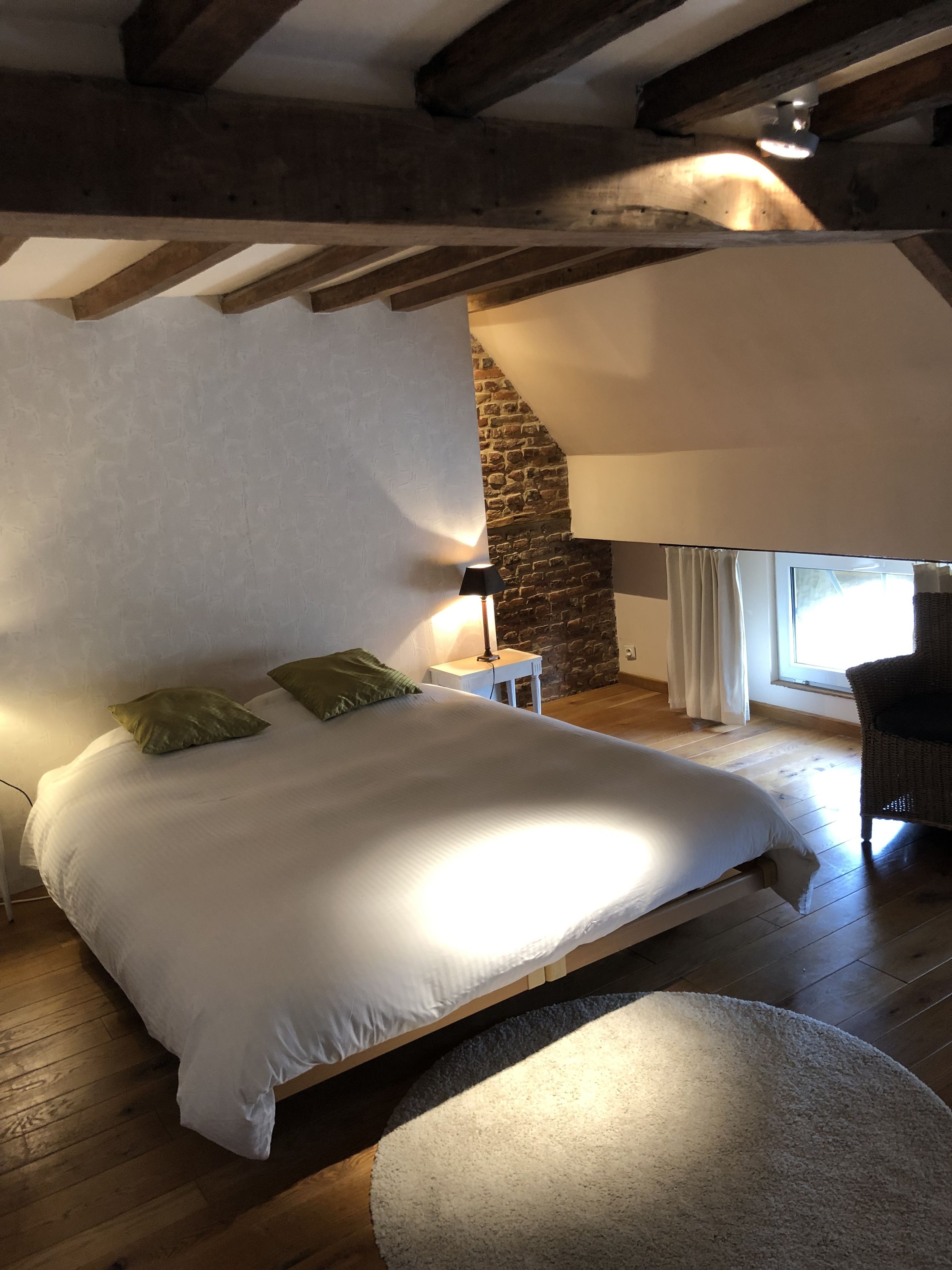 Ein Schlafzimmer mit einem großen Bett, einem Nachttisch, einer Lampe, einem Sessel und einer Steinwand.