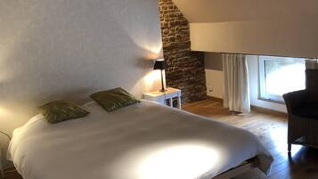 Ein Schlafzimmer mit einem großen Bett, einem Nachttisch, einer Lampe, einem Sessel und einer Steinwand.