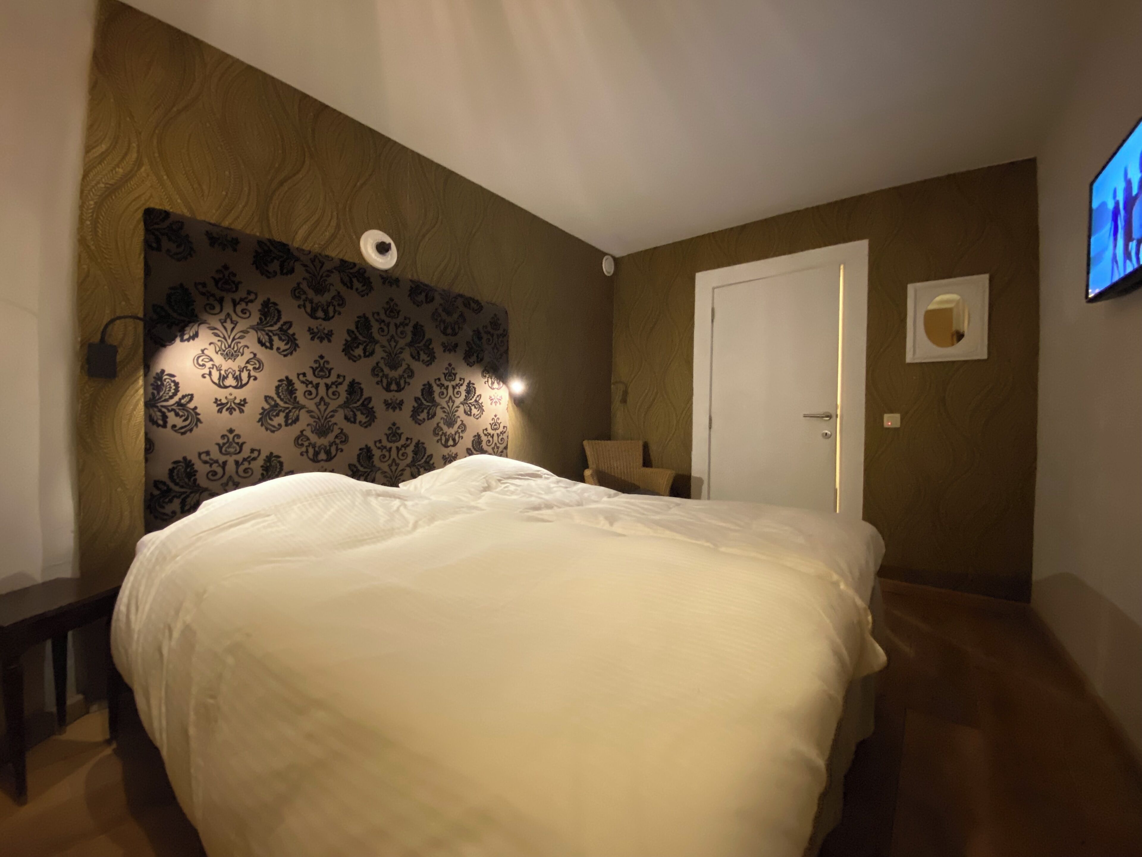A bedroom with a large bed, a chair, a wall-mounted TV, and a door.