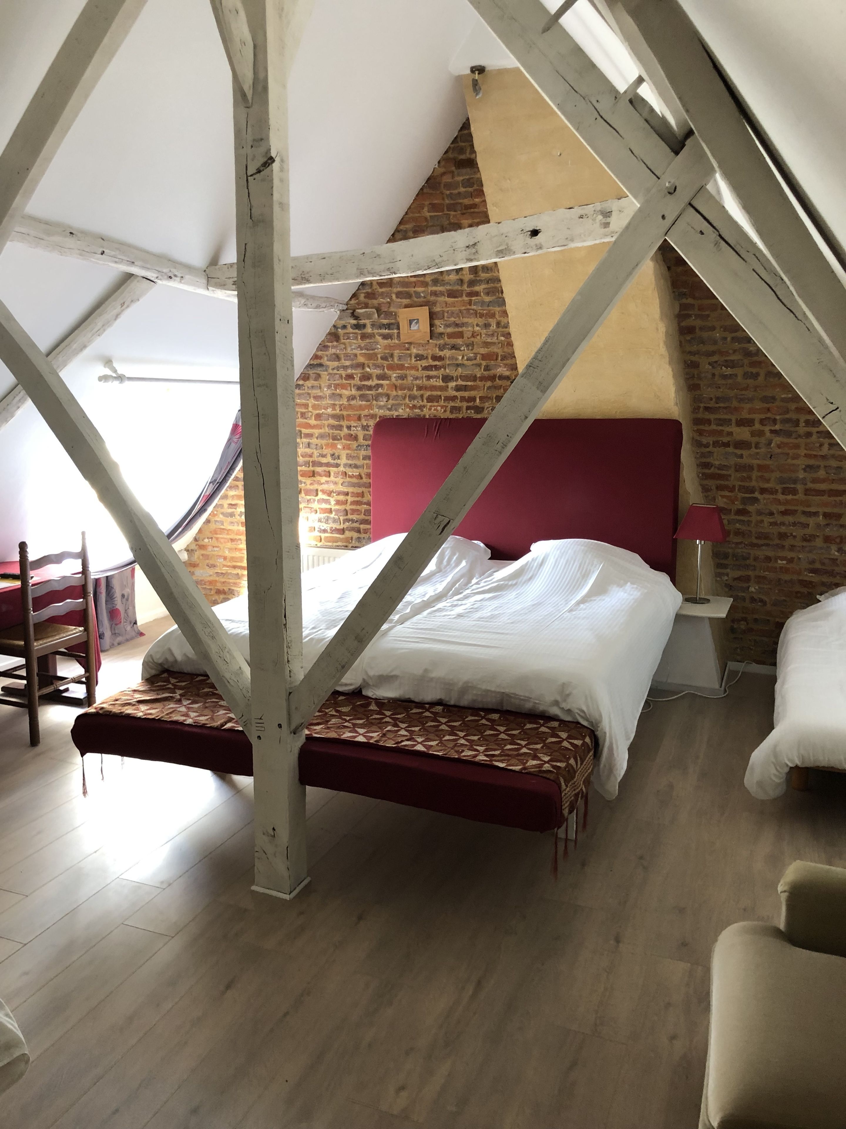 A loft bedroom with exposed wooden beams, a brick wall, a red headboard, and a wooden floor.