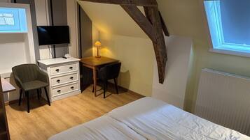 A bedroom with a bed, a desk with a chair, a TV, and a lamp.