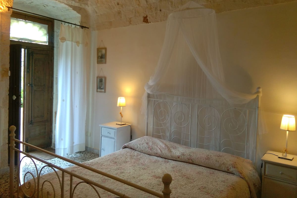 A bedroom with a bed, two bedside tables with lamps, a window with curtains, and a door.