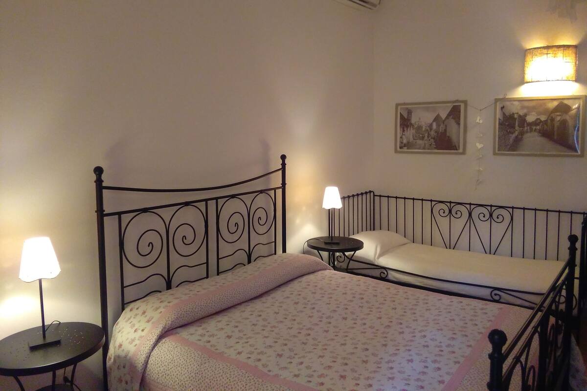 A single bed with a metal frame, a bedside table with a lamp, and a wall-mounted air conditioning unit.