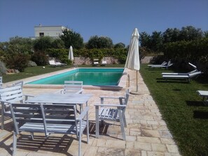 A swimming pool with lounge chairs and umbrellas, surrounded by a stone patio and greenery. - Masseria Sant'Angelo (Monopoli)