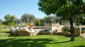 Un parque con un banco de piedra, un área de juegos y un muro de piedra.