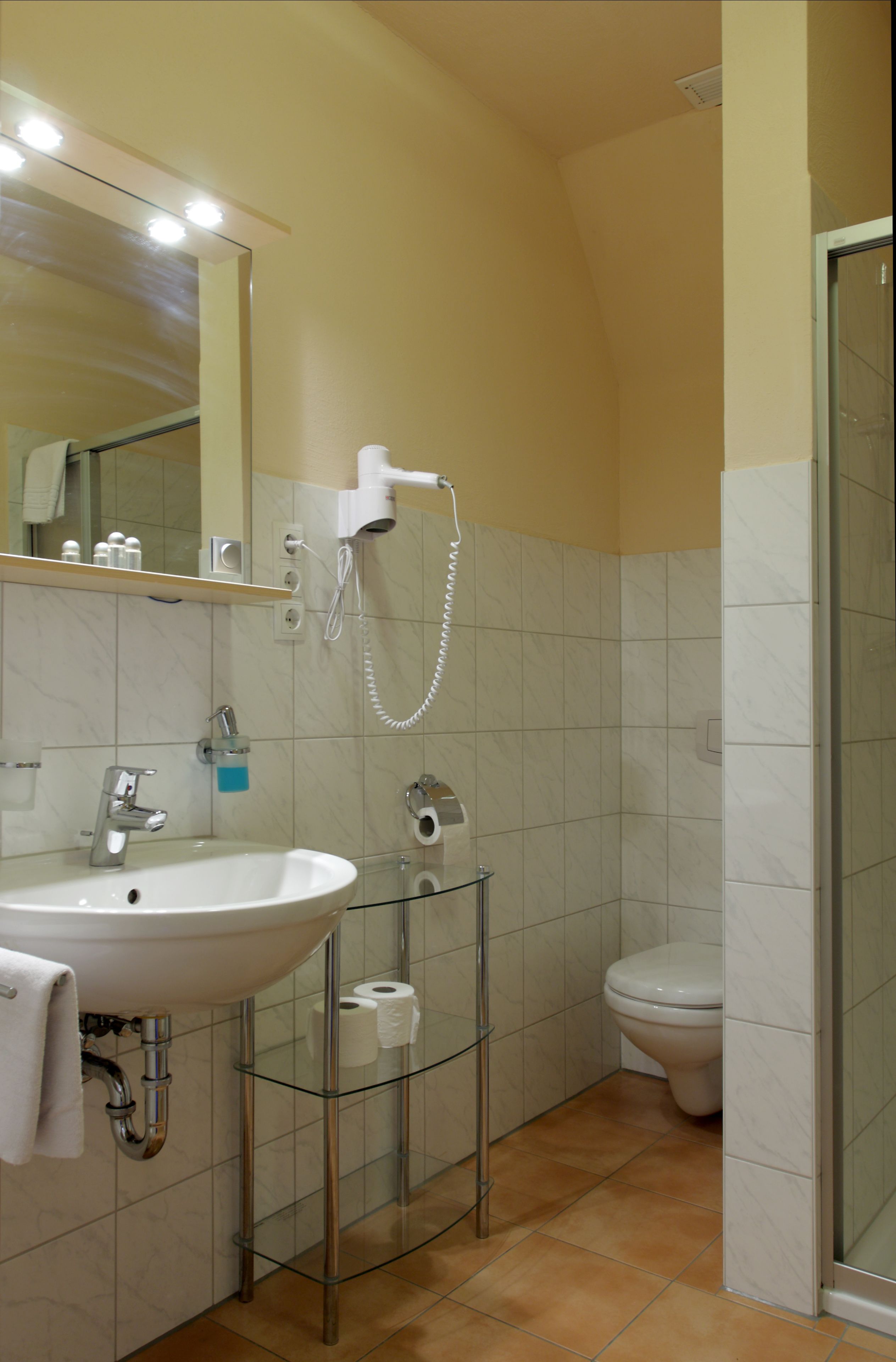 Ein Badezimmer mit weißem Waschbecken, Spiegel und einer Duschkabine aus Glas.