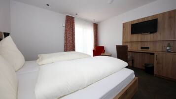 A hotel room with a large bed, a TV mounted on the wall, a wooden desk, and a red chair.