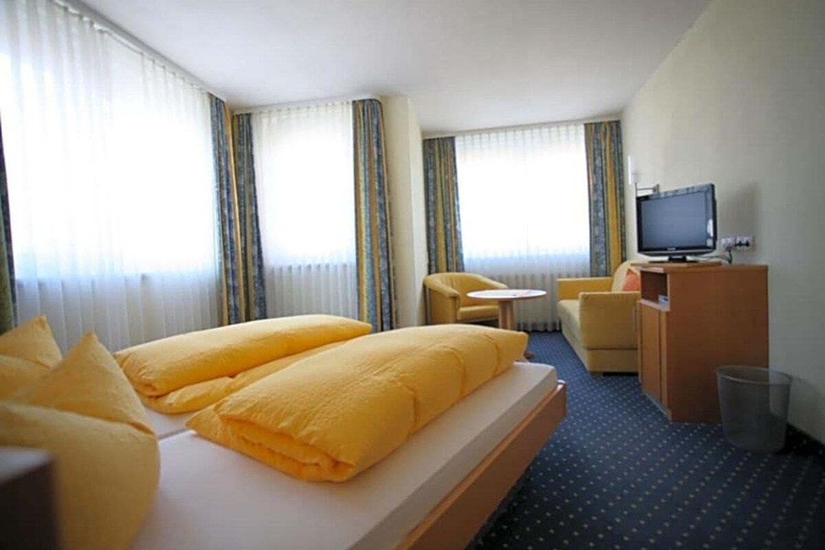 A hotel room with a bed, a desk, a chair, a television, and a small table.