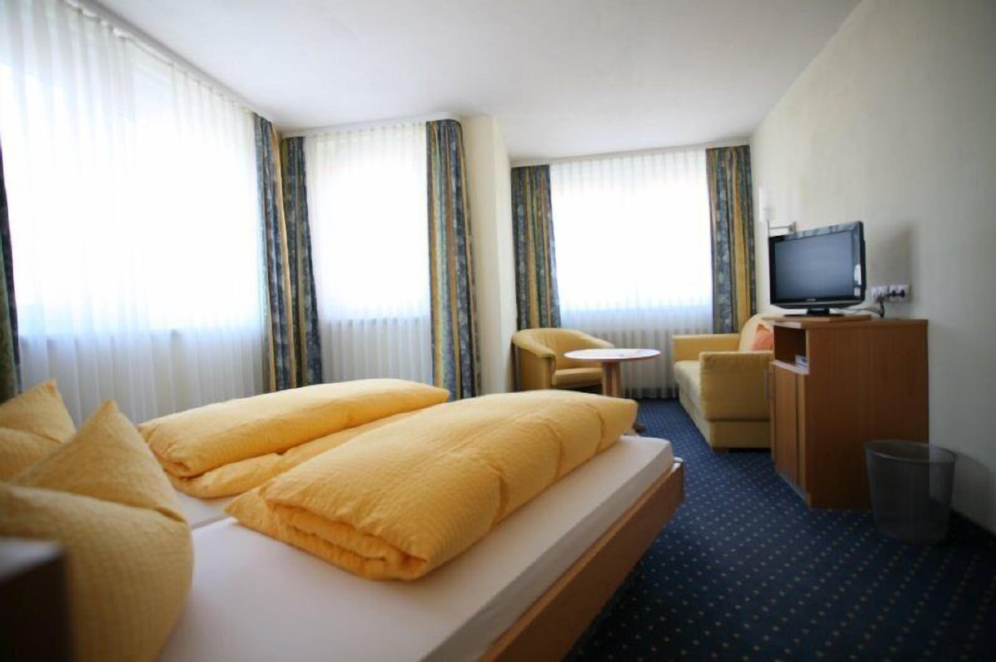Ein Hotelzimmer mit einem Bett, zwei gelben Kissen, einem Schreibtisch mit Computer, einem Stuhl und einem Fernseher.