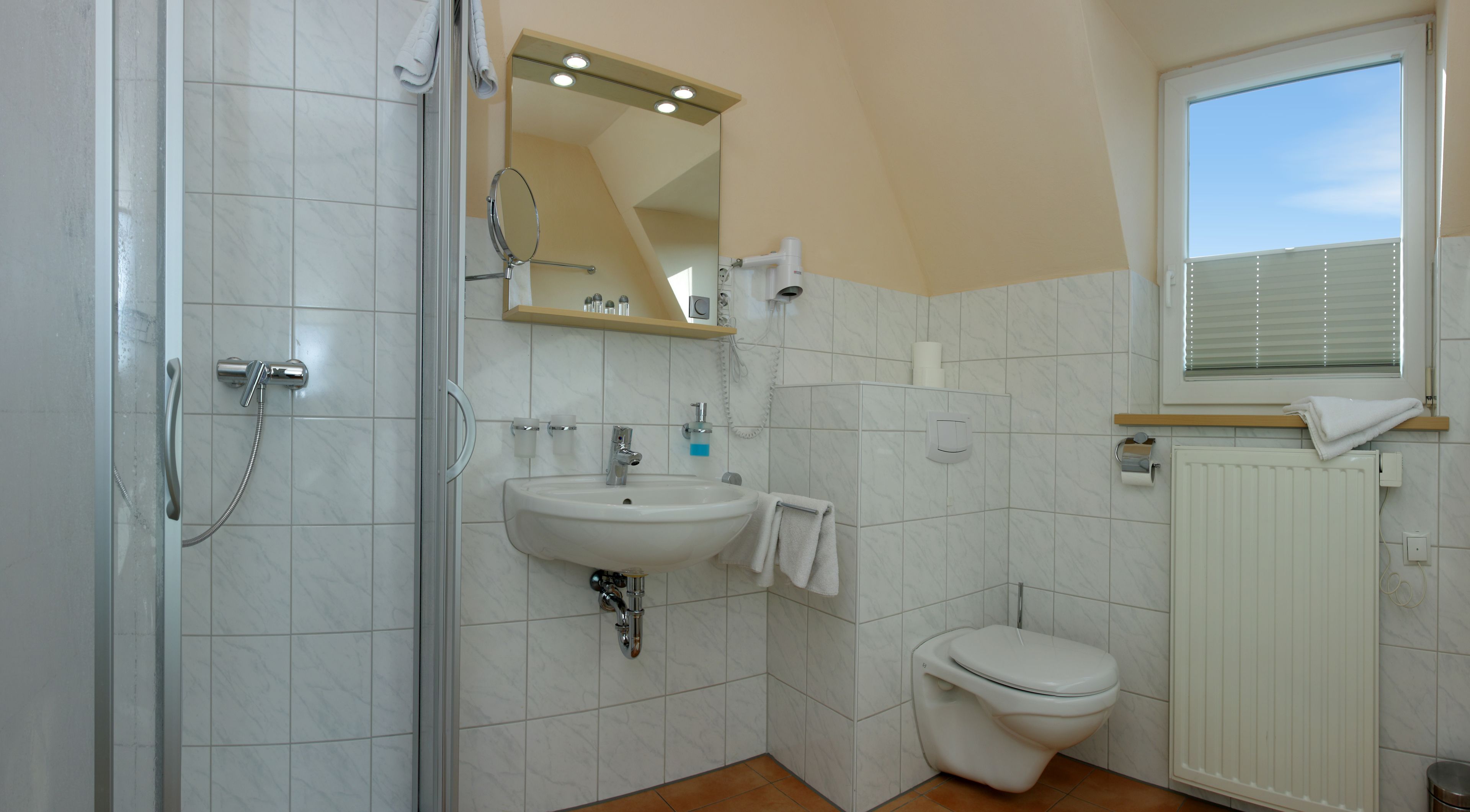 Un baño con ducha de vidrio, un lavamanos con espejo, un inodoro y una ventana con persianas.