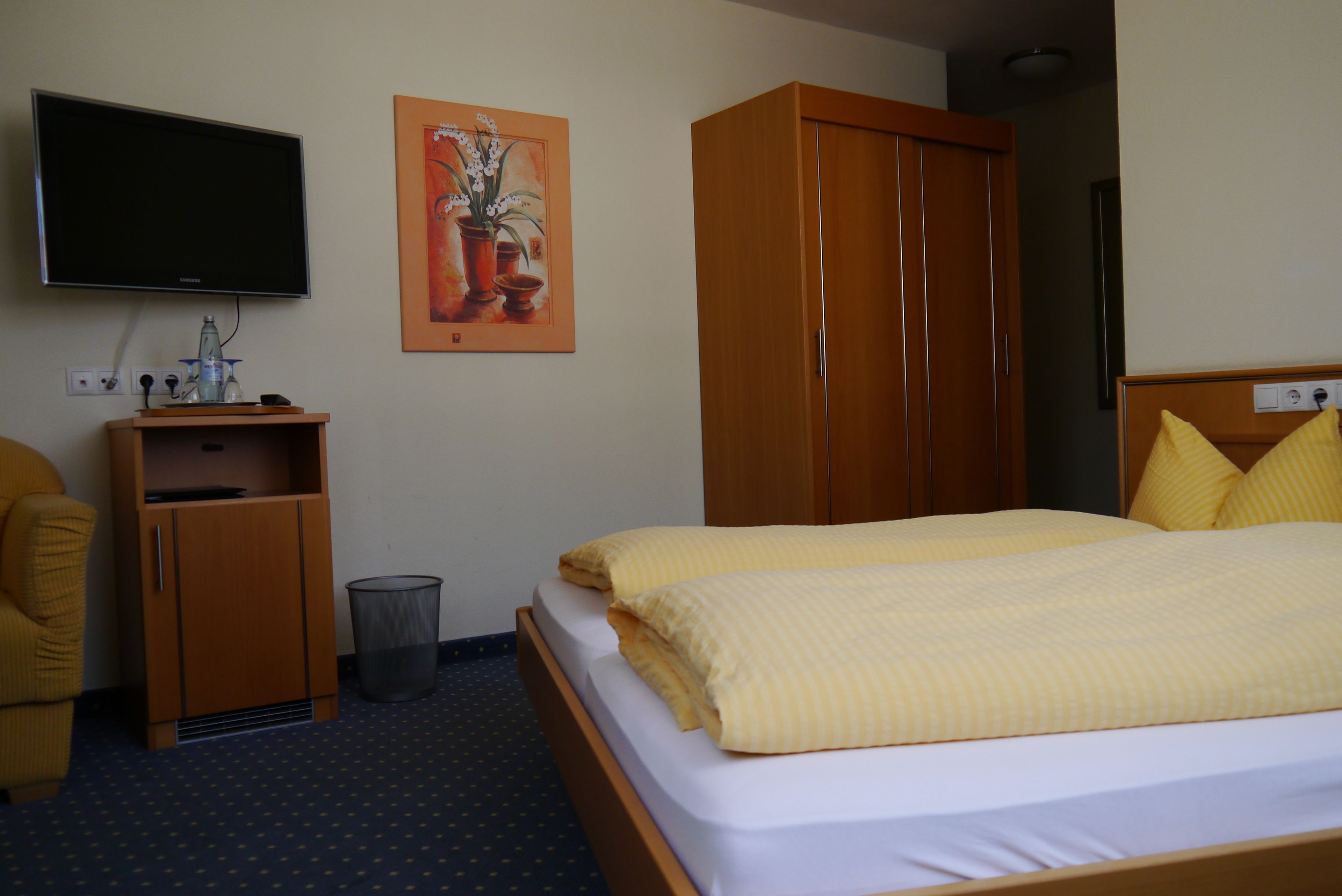 Ein Hotelzimmer mit Bett, Wandfernseher, Holzschrank und Nachttisch mit Lampe.
