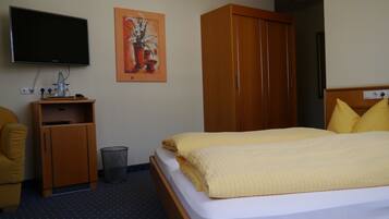 Ein Hotelzimmer mit Bett, Wandfernseher, Holzschrank und Nachttisch mit Lampe.
