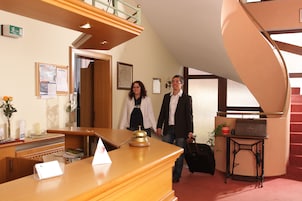 Zona de recepción con un escritorio de madera, un timbre, un letrero, una escalera y una pequeña mesa con una maleta.