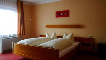 A hotel room with a wooden bed, white bedding, a red artwork above the bed, and a window with curtains.