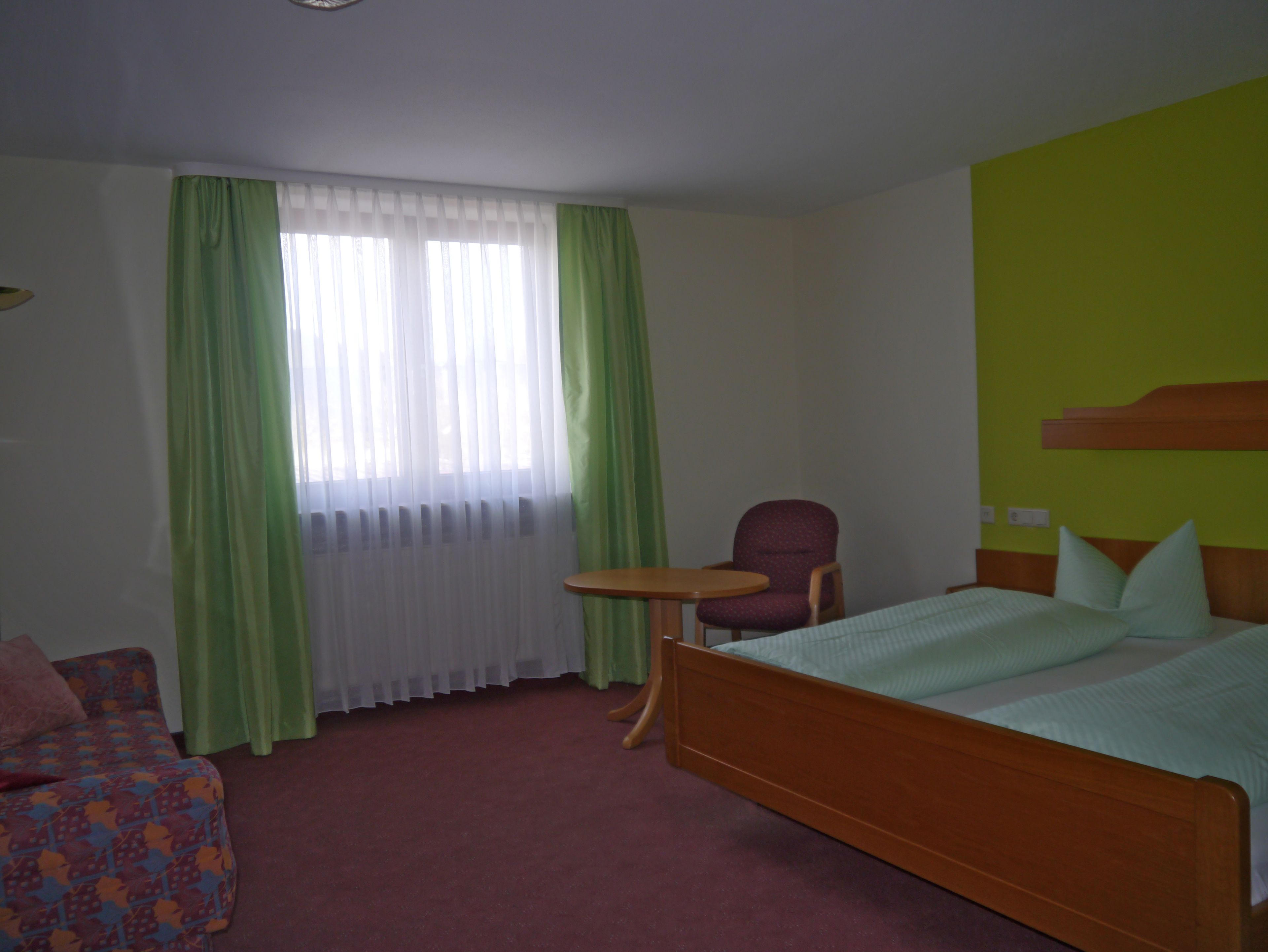 A hotel room with a bed, a chair, a small table, and a sofa.