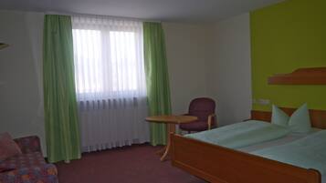 A hotel room with a bed, a chair, a small table, and a sofa.