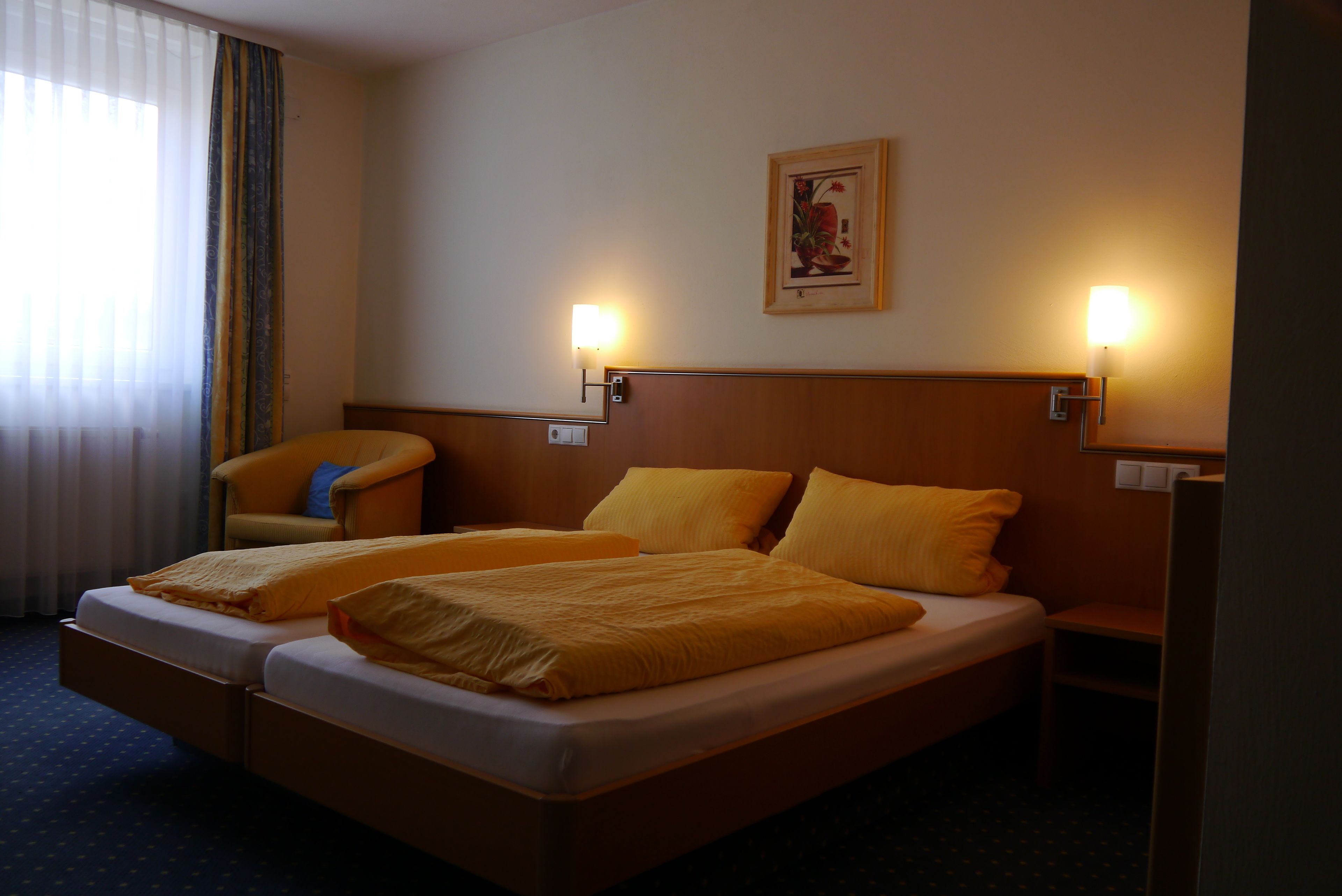 A hotel room with a double bed, two bedside tables, a chair, and a wall-mounted light fixture.