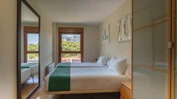 Habitación de hotel con dos camas, un espejo grande y vistas a zonas verdes y edificios.
