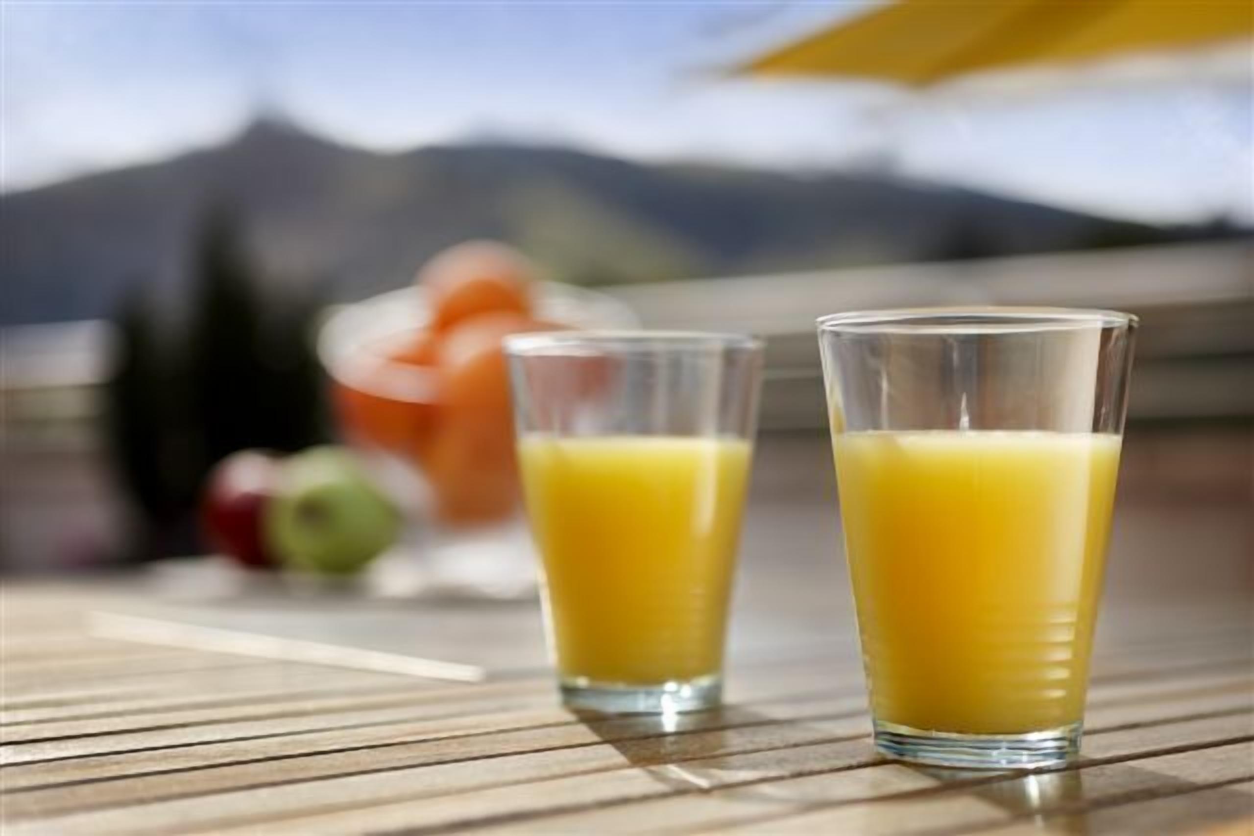 Due bicchieri di succo d'arancia su un tavolo di legno, con vista sulle montagne sullo sfondo.