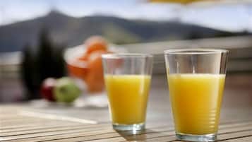 Two glasses of orange juice on a wooden table with a mountain view in the background.