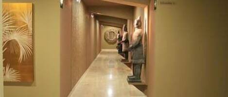 A hotel hallway with a marble floor, a large abstract wall art piece on the left, and a statue on the right.