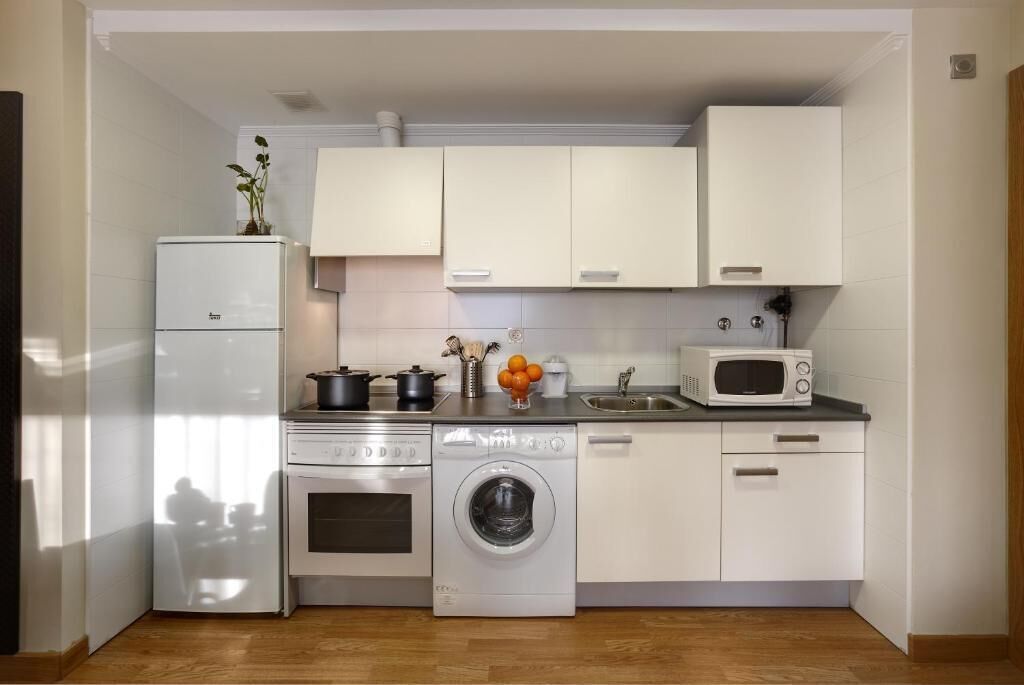A compact kitchen with a refrigerator, stove, microwave, and washing machine.