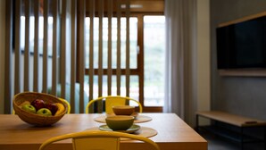 A dining area with a wooden table, yellow chairs, a woven fruit basket, and a television mounted on the wall. - Spirit Apartamentos Atxuri (Bilbao)