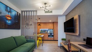 A modern living room with a green sofa, a dining area with a wooden table and yellow chairs, a kitchen in the background, and a mounted TV on the wall. - Spirit Apartamentos Atxuri (Bilbao)