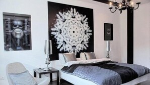 A modern bedroom with a large bed, a chair, a side table, and a chandelier.
