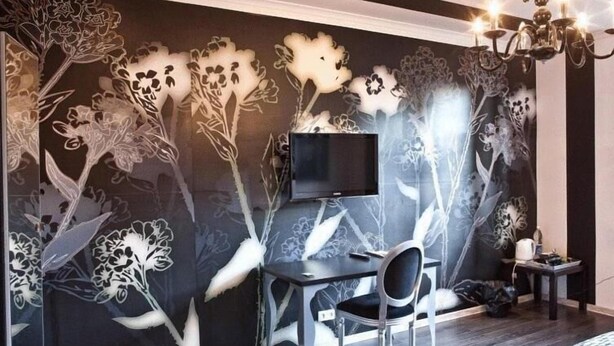 A modern bedroom with a dark floral mural, a flat-screen TV, a desk with a chair, and a chandelier.