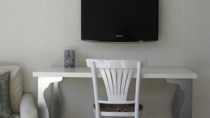 A white chair with a cat, a white table, and a black TV mounted on the wall.