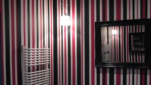 A striped wall with a white radiator and a black-framed mirror.