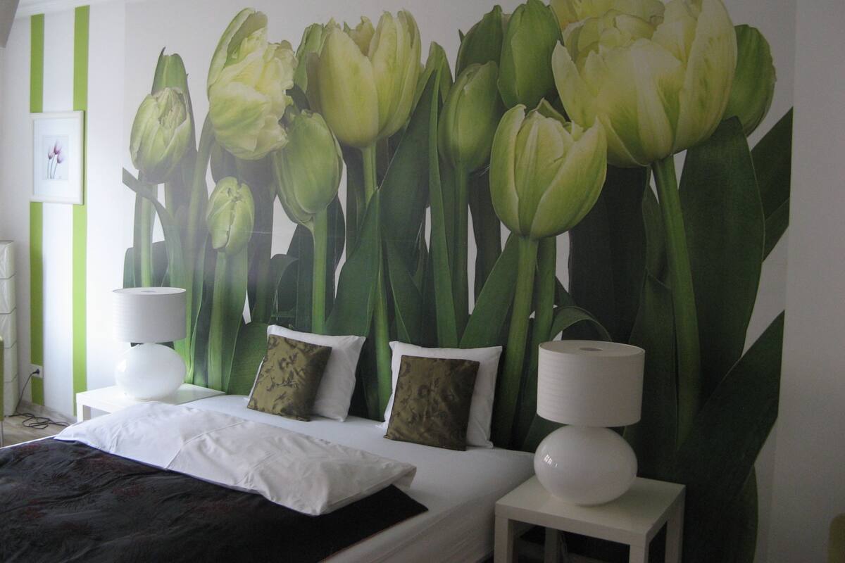A hotel room with a large floral mural on the wall, a bed with white bedding, and two bedside tables with lamps.