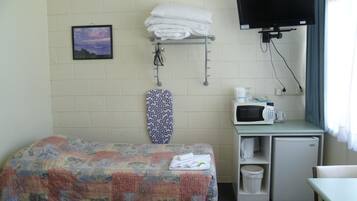 A small hotel room with a bed, a TV, a microwave, and a small table.