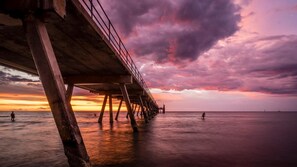 A pier extending over calm waters during sunset with a dramatic sky.