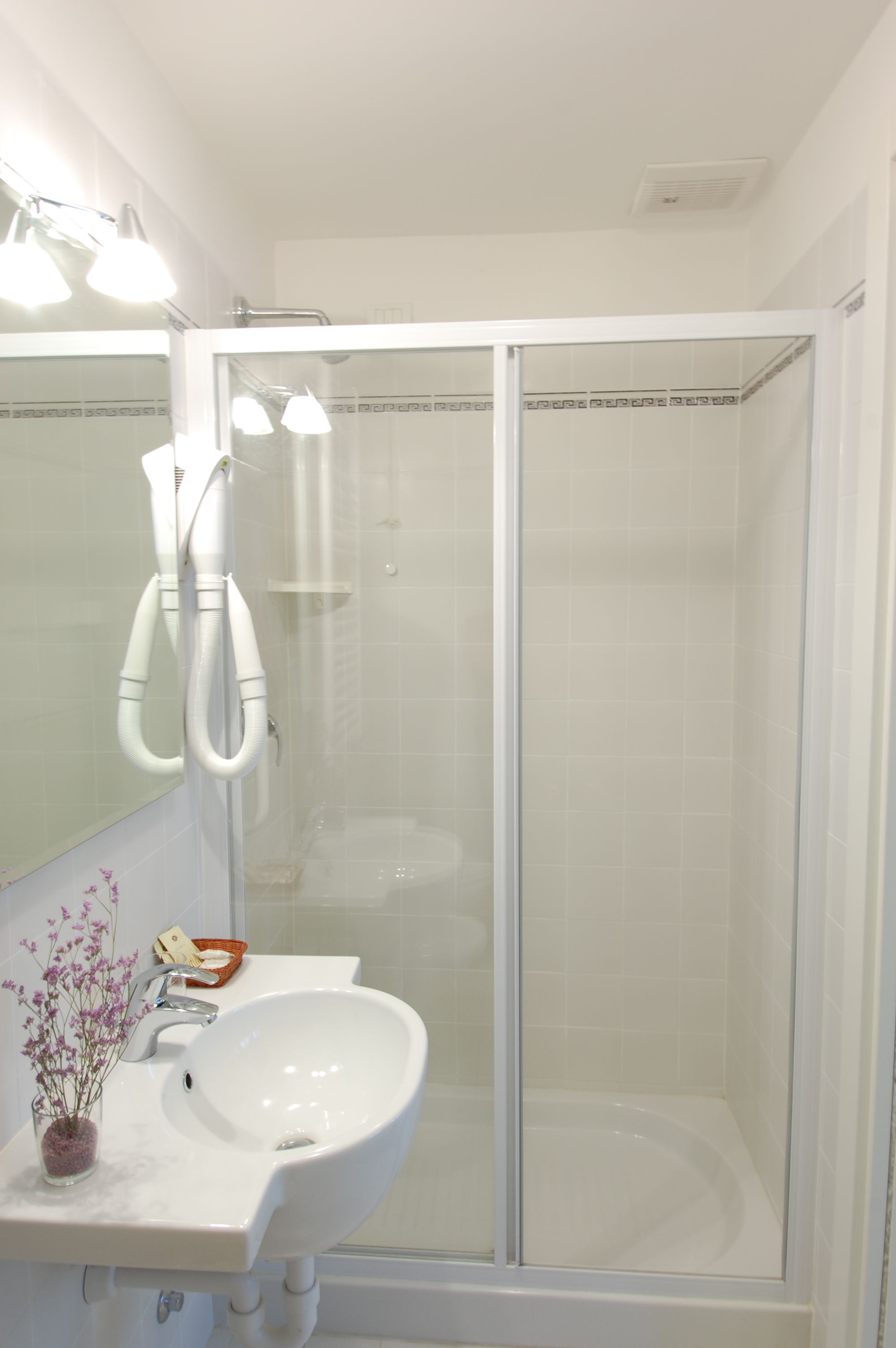 Un baño con lavamanos blanco, cabina de ducha de vidrio y espejo con iluminación.