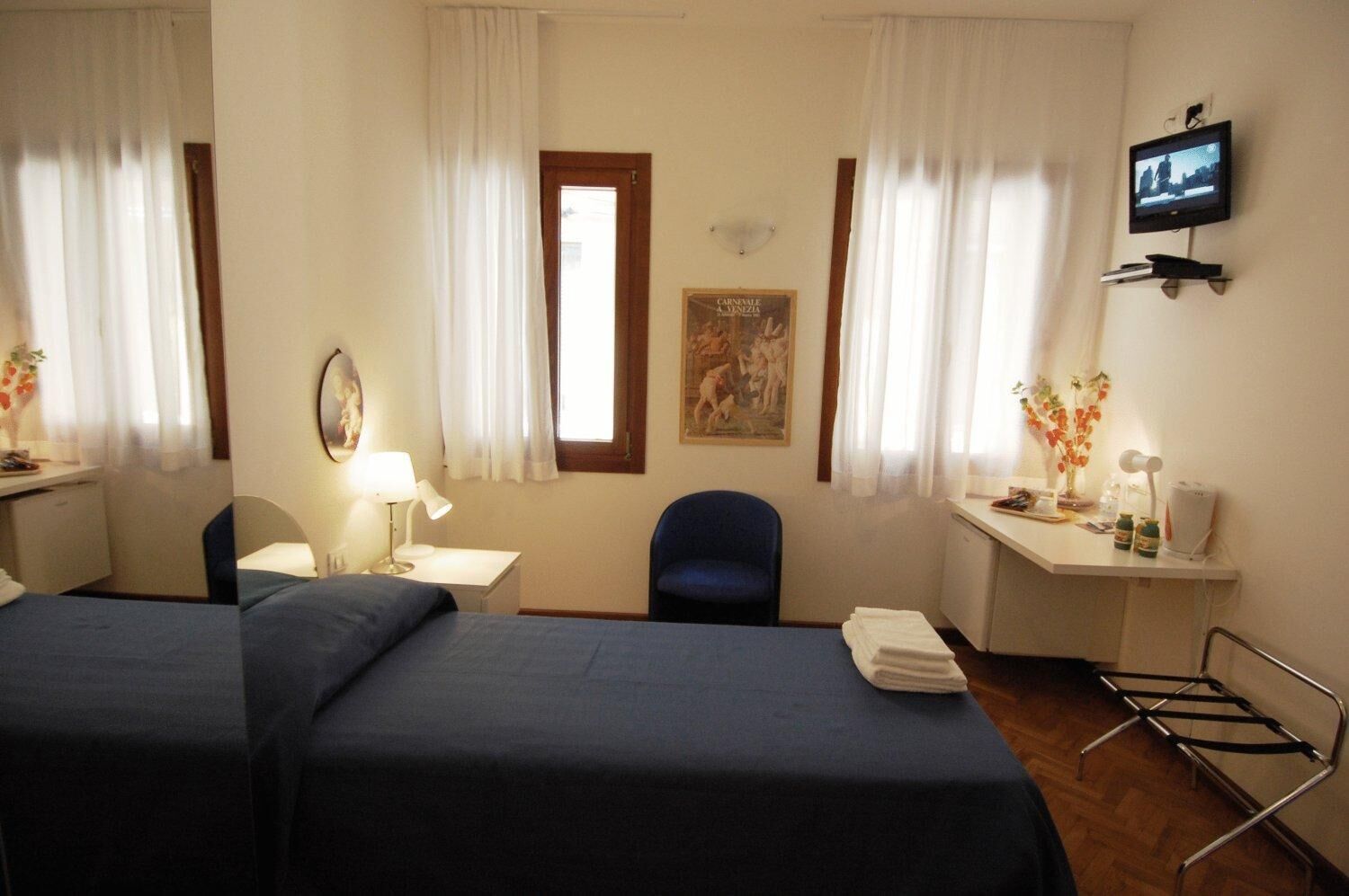 A hotel room with two beds, a desk with a lamp, a chair, a TV mounted on the wall, and a window with curtains.