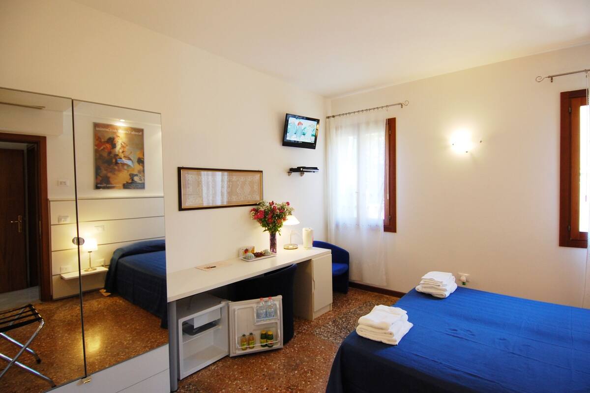 Een hotelkamer met een bed, een bureau, een stoel, een televisie en een kleine koelkast.