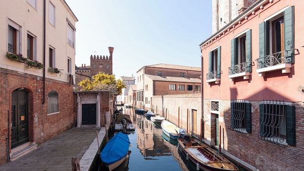 A narrow canal with boats docked along the sides, surrounded by historic buildings with brick facades and traditional shutters. - Santa Margherita Guesthouse (Venice)