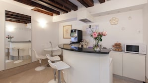 A modern kitchen with white cabinetry, a central island with bar stools, a microwave, and a refrigerator. - Santa Margherita Guesthouse (Venice)