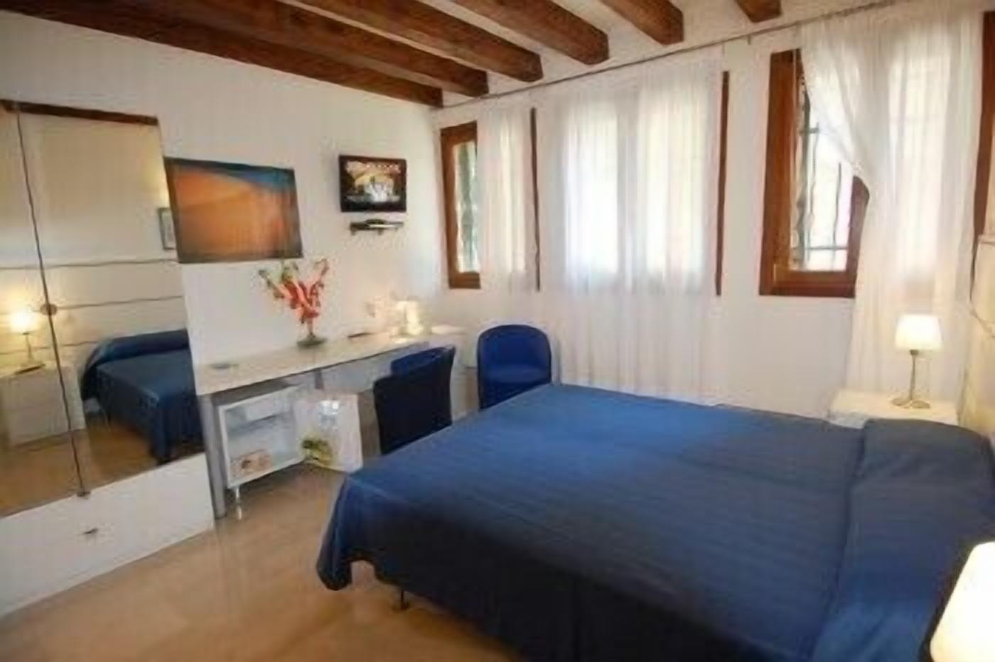 A bedroom with a bed, a desk, a chair, a mirror, and a window with curtains.