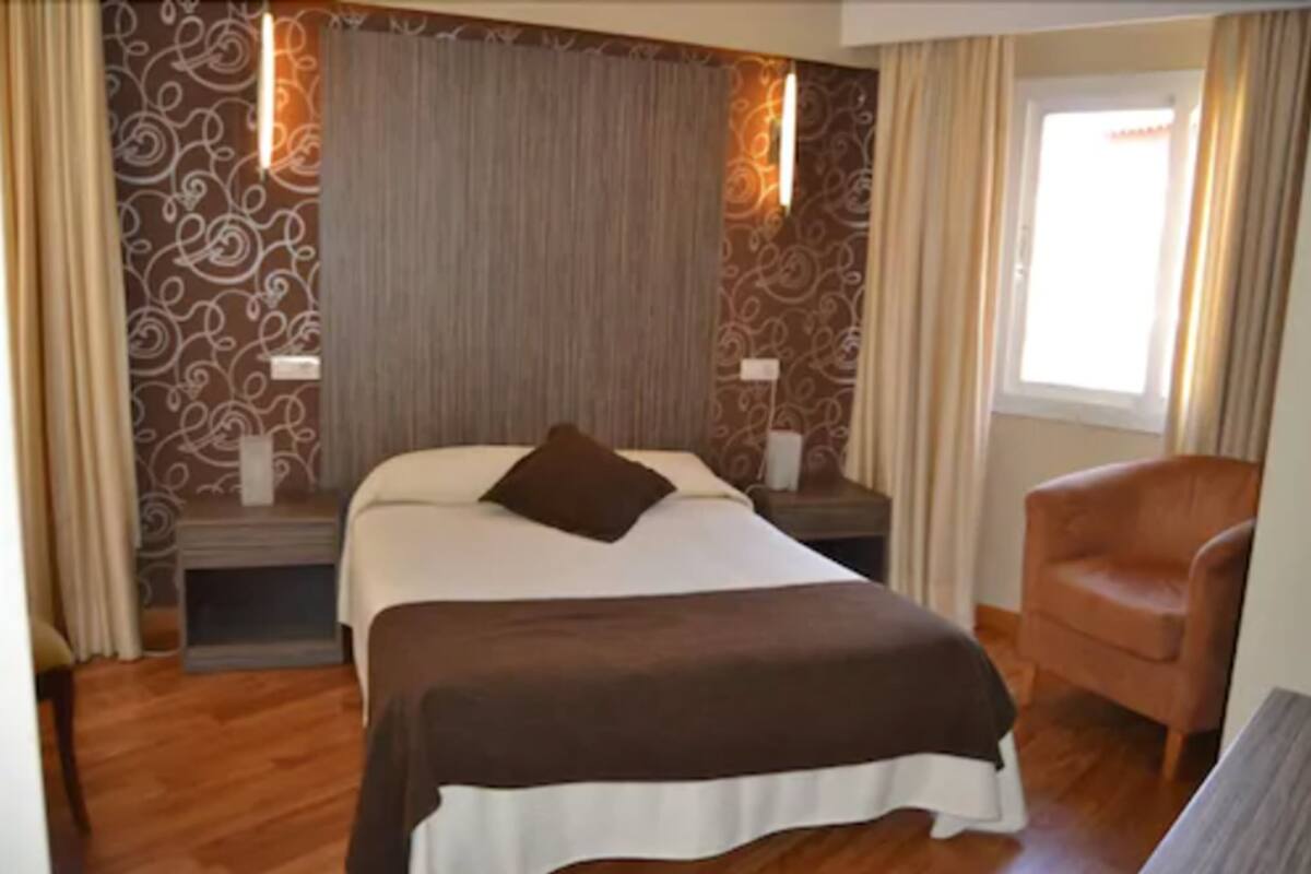 Une chambre d’hôtel avec un lit, une chaise, une table de chevet et une fenêtre.