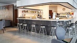 A modern bar area with a curved counter, multiple stools, and a variety of bar tools and bottles. - Hotel Costamar (Torrox)